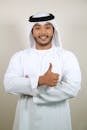 Portrait of a smiling man in traditional Emirati clothing giving a thumbs up against a white background.